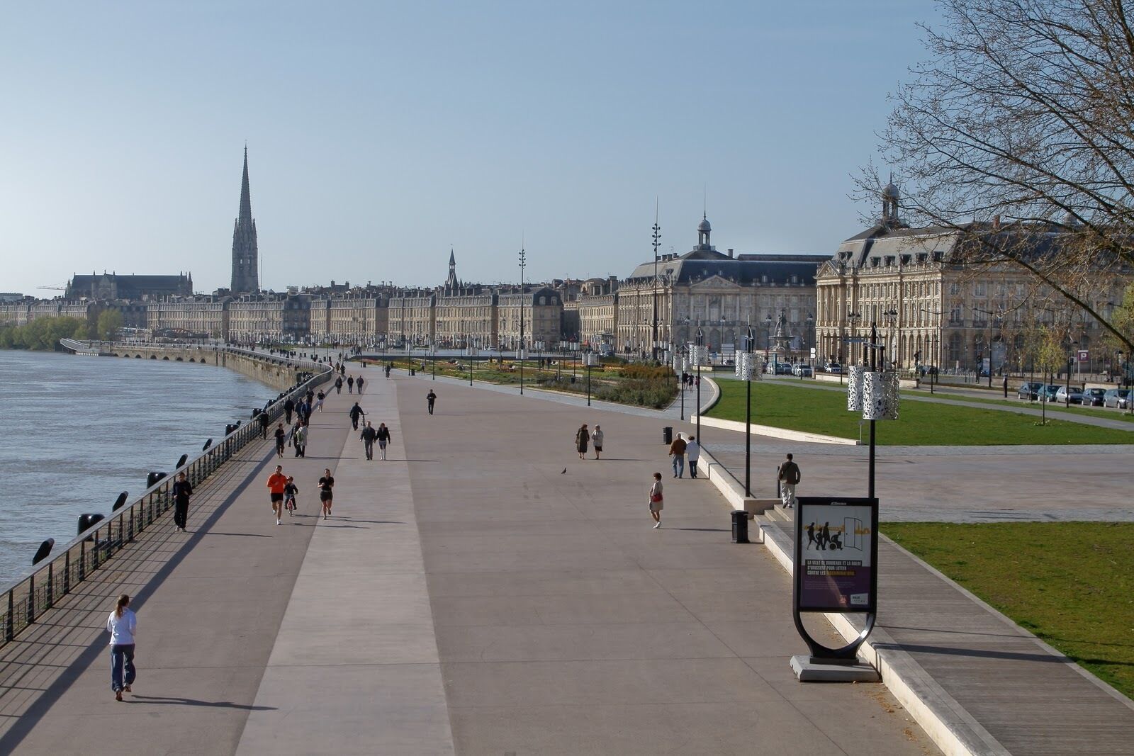 A wide promenade with a river on one side and buildings on the other.