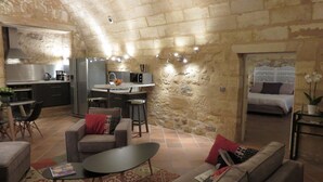 A cozy living area with a stone wall, a kitchen with modern appliances, and a bedroom with a bed and nightstand. - Great warm T2 68 M2, atypical, in the historic center (Bordeaux)