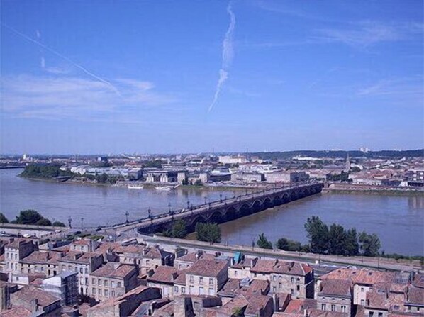 Panoramic city view with a historic bridge spanning a wide river, surrounded by a mix of traditional and modern buildings.