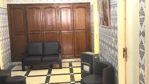 Una habitación con un armario de madera, un sofá negro, una mesita pequeña y un papel tapiz estampado.