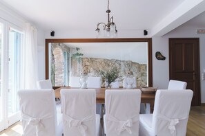 A dining area with a large mirror, white chairs, a wooden table, and a chandelier.