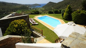 Piscina con vistas al mar, rodeada por un muro de piedra y una zona ajardinada con tumbonas.