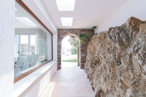 A corridor with a stone wall, a large window, and an archway leading to an outdoor area.