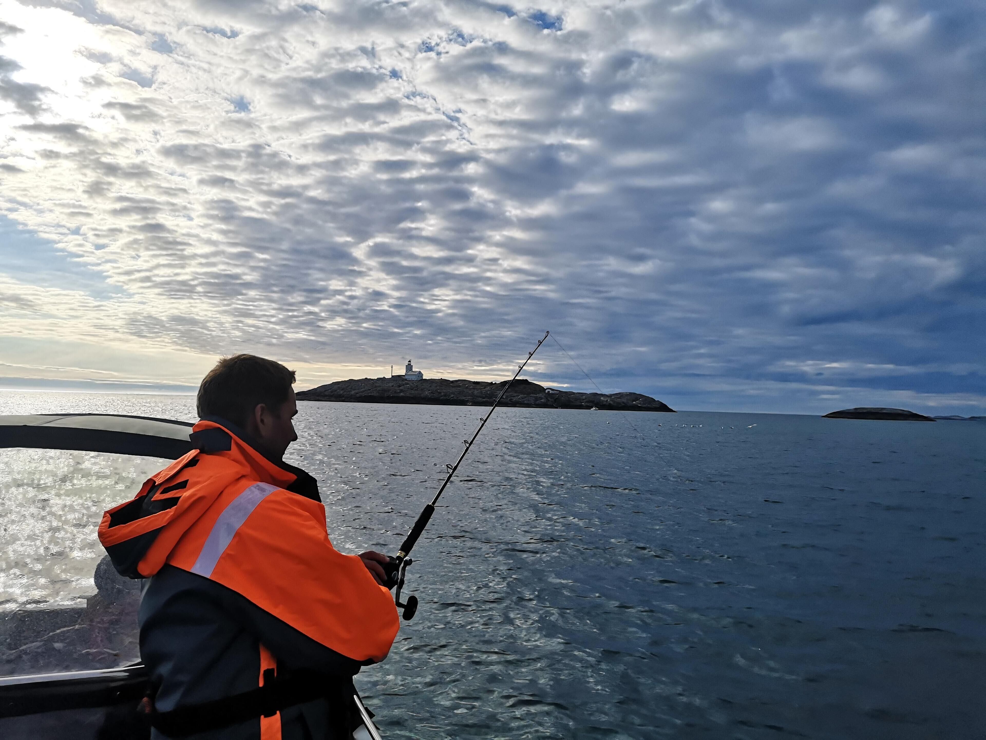 Une personne pêchant sur un bateau, avec une île rocheuse en arrière-plan.