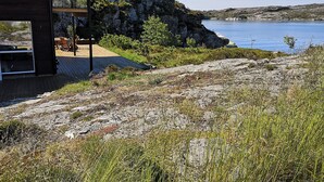 A modern house with a deck overlooking a lake, surrounded by rocky terrain and greenery.
