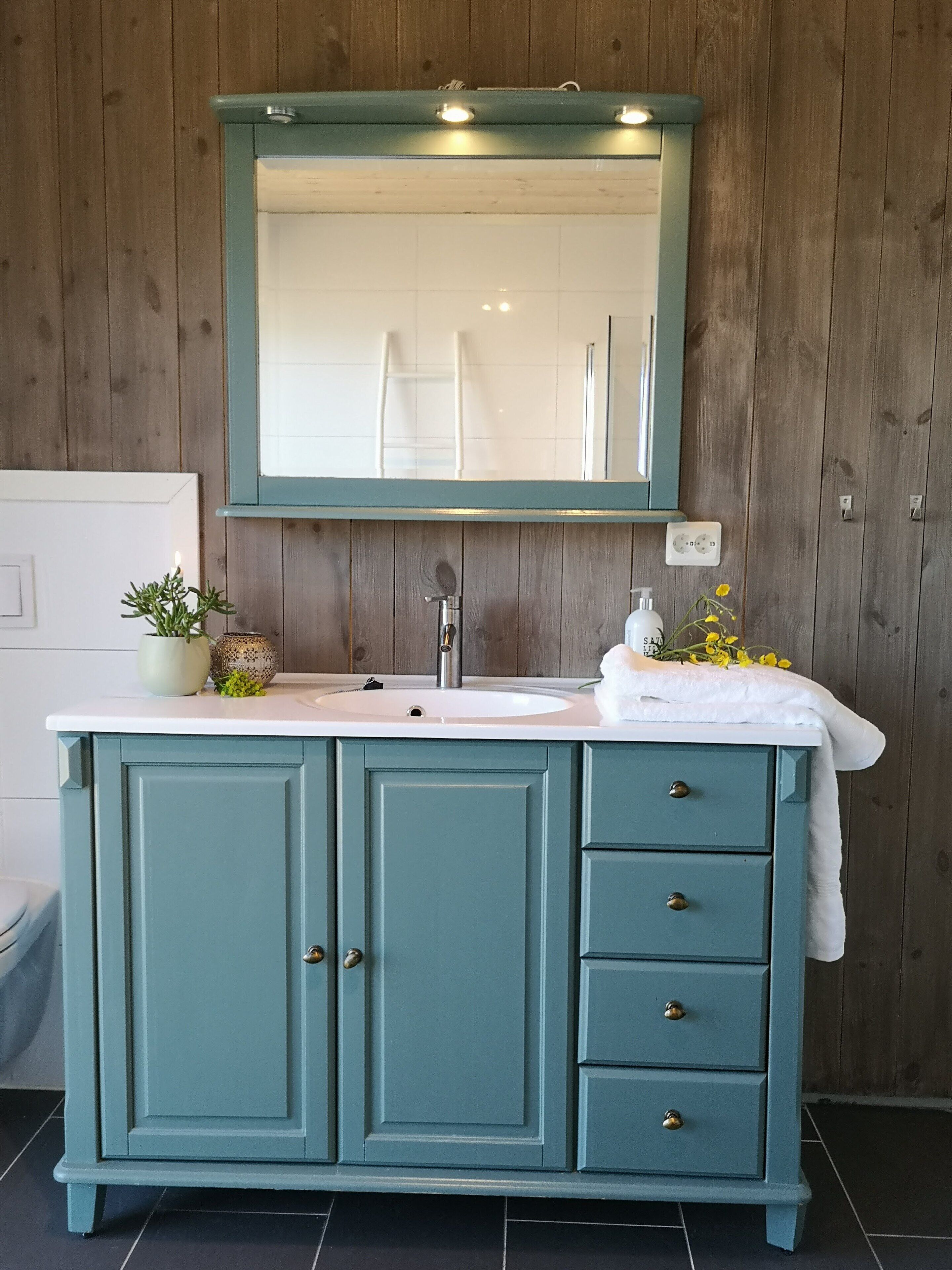 A bathroom with a teal vanity, a mirror, and a sink.