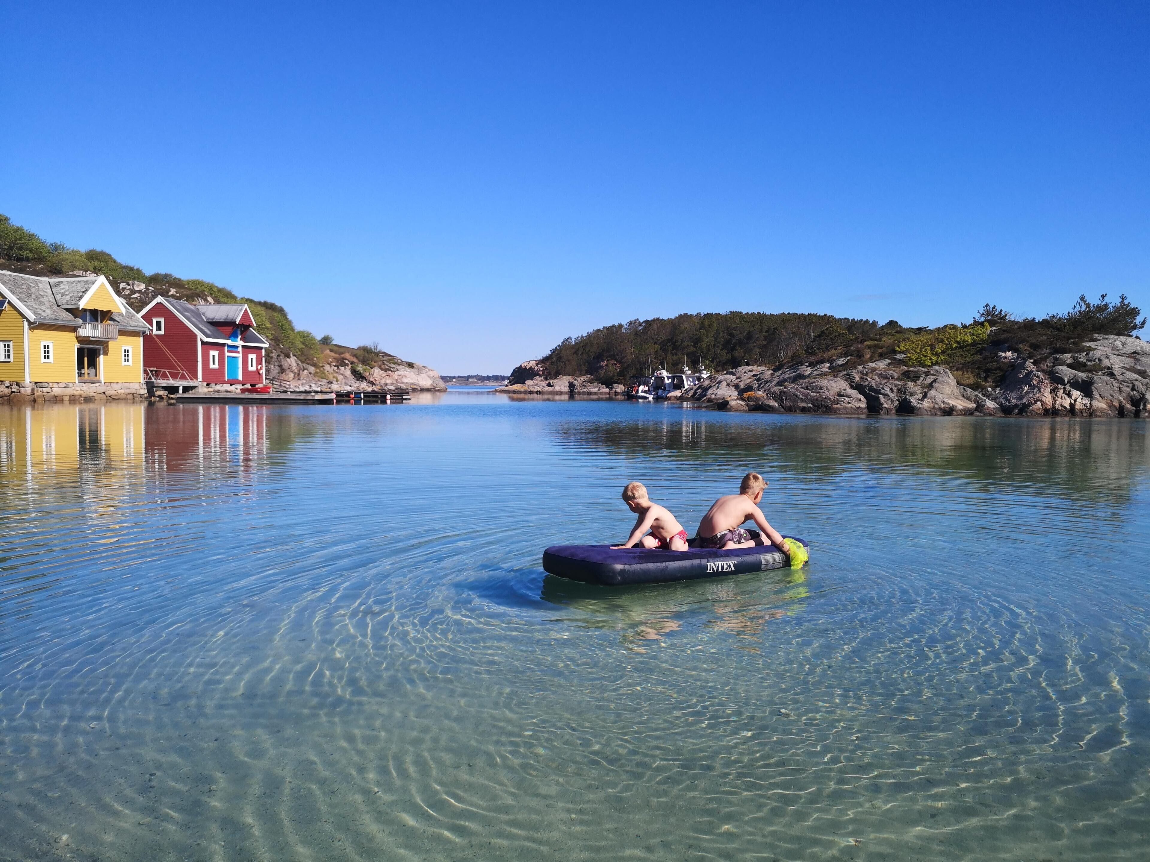 A calm water body with houses on the left and a rocky shore on the right.