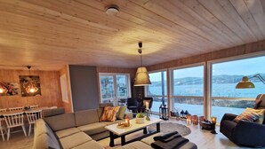 A cozy living room with a large sectional sofa, a dining table, and a view of the sea through large windows.