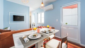 A dining area with a table set for two, a television mounted on the wall, and a window with striped curtains. - Victoria Project - Apartment II - Private Parking (Porto)