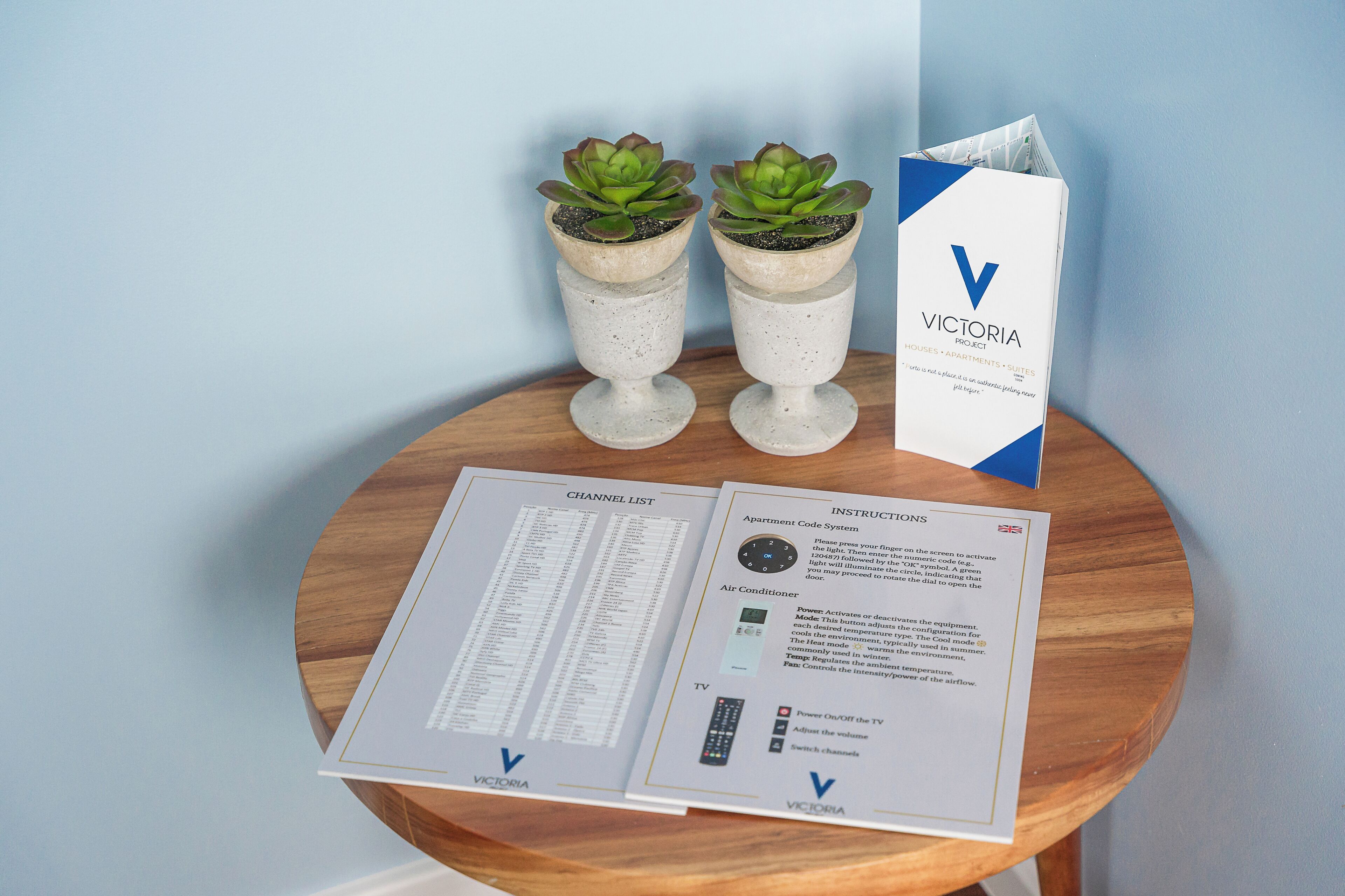Une brochure présentant les appartements du projet Victoria, avec une liste des chaînes de télévision et des instructions, est posée sur une table en bois.