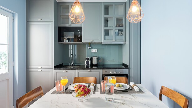 A modern kitchen with grey cabinets, a black countertop, and a dining table set with plates, glasses, and a fruit centerpiece. - Victoria Project - Apartment II - Private Parking (Porto)