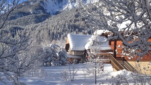 Paesaggio montano innevato con una baita di legno e un pontile in legno.