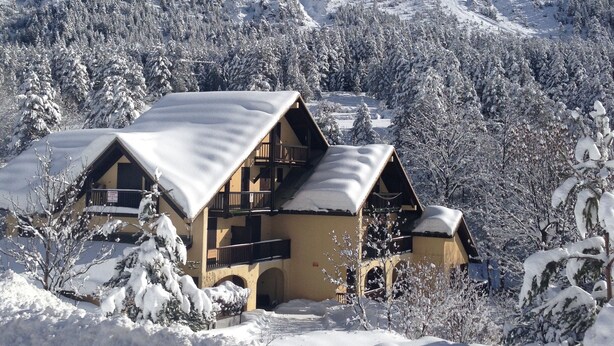 Un edificio in stile chalet con tetto spiovente, circondato da alberi e montagne innevate.