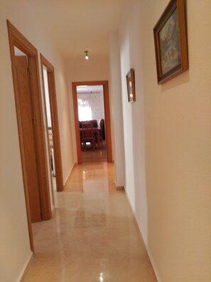 A hallway with wooden doors, a framed picture on the wall, and a view into a dining area with a table and chairs.