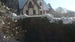 Una iglesia con un techo empinado y una aguja alta, rodeada de árboles cubiertos de nieve y un muro de piedra.
