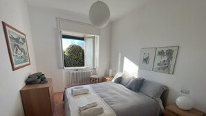 Un dormitorio con una cama grande, un radiador, una ventana con vistas a zonas verdes y obras de arte en las paredes.