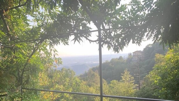 Un balcón con vistas a un valle boscoso, una mecedora de madera y una silla verde.