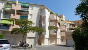 Un immeuble résidentiel à plusieurs étages, doté de balcons, d’un espace de stationnement et d’un vélo garé devant.