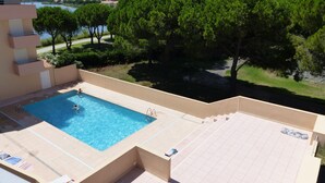 Une piscine où se trouvent deux personnes, entourée d’une terrasse carrelée et offrant une vue sur une étendue d’eau et des arbres.