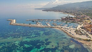An aerial view of a coastal town with a marina, clear blue waters, and a mountainous backdrop. - Blue House with pool. Paradise between sky and sea  (Trabia)