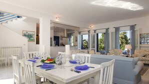 A dining area with a white table set for six, blue plates, and clear glasses. There is a blue sofa and a white chair in the background. - Blue House with pool. Paradise between sky and sea  (Trabia)
