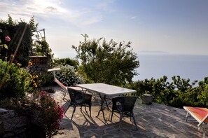 An outdoor patio with a stone table and chairs, surrounded by lush greenery and a view of the sea. - Vigna Maria Vacation Rentals (Zanca)