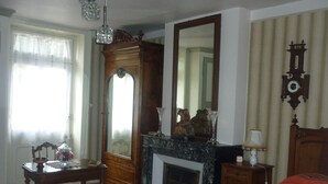 A bedroom with a wooden bed, a nightstand, a dresser, a mirror, a chandelier, and a fireplace. - Beautiful family home (Vauban)