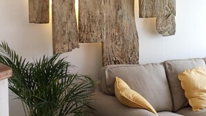 A living room with a sofa, a large wooden wall art piece, a potted plant, and a wicker chair. -  Charming riverside stone built  property in Perigord (La Roque-Gageac)