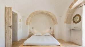 Une chambre à coucher minimaliste avec un lit en bois, un plafond en pierre en forme d’arc et une simple table de chevet avec une lampe.