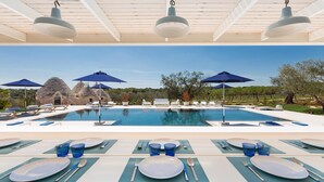 Un espace de restauration aménagé au bord de la piscine, avec des tables pour deux, offrant une vue sur la piscine et un bâtiment en pierre.