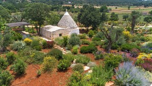 Un bâtiment en pierre surmonté d’un toit conique, entouré d’un jardin où poussent différentes plantes et fleurs.