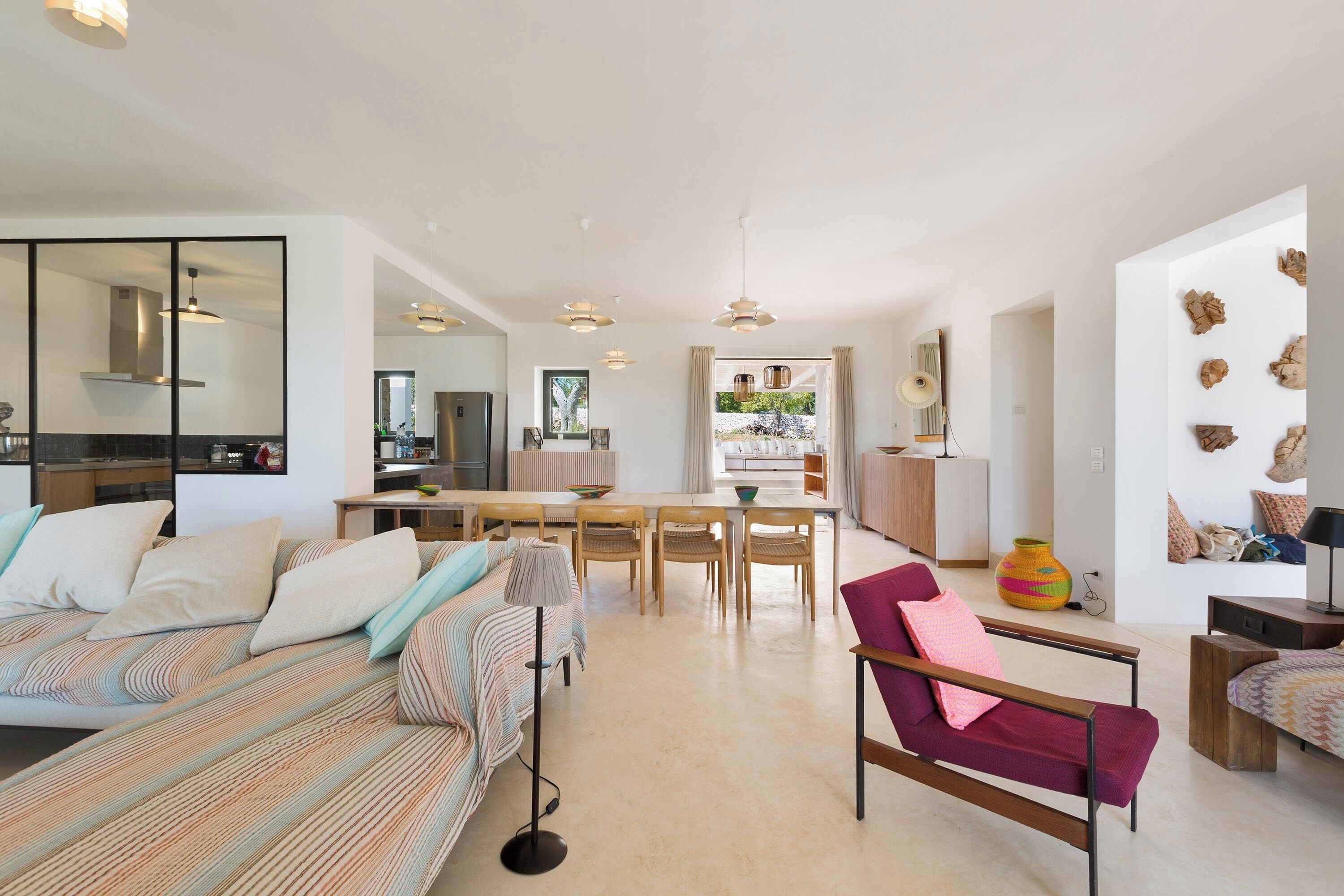 A modern living room with a sofa, armchairs, a dining table, and a kitchen in the background.