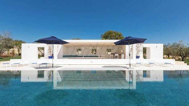 Un espace piscine extérieur moderne, avec une eau d’un bleu limpide, des chaises longues blanches et des parasols.