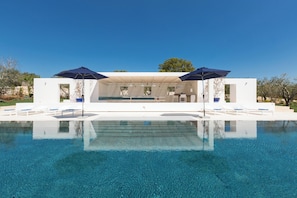 A modern outdoor pool area with clear blue water, white lounge chairs, and umbrellas.