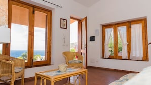 Ein Zimmer mit großen Fenstern, Korbmöbeln, Fliesenboden und Meerblick.