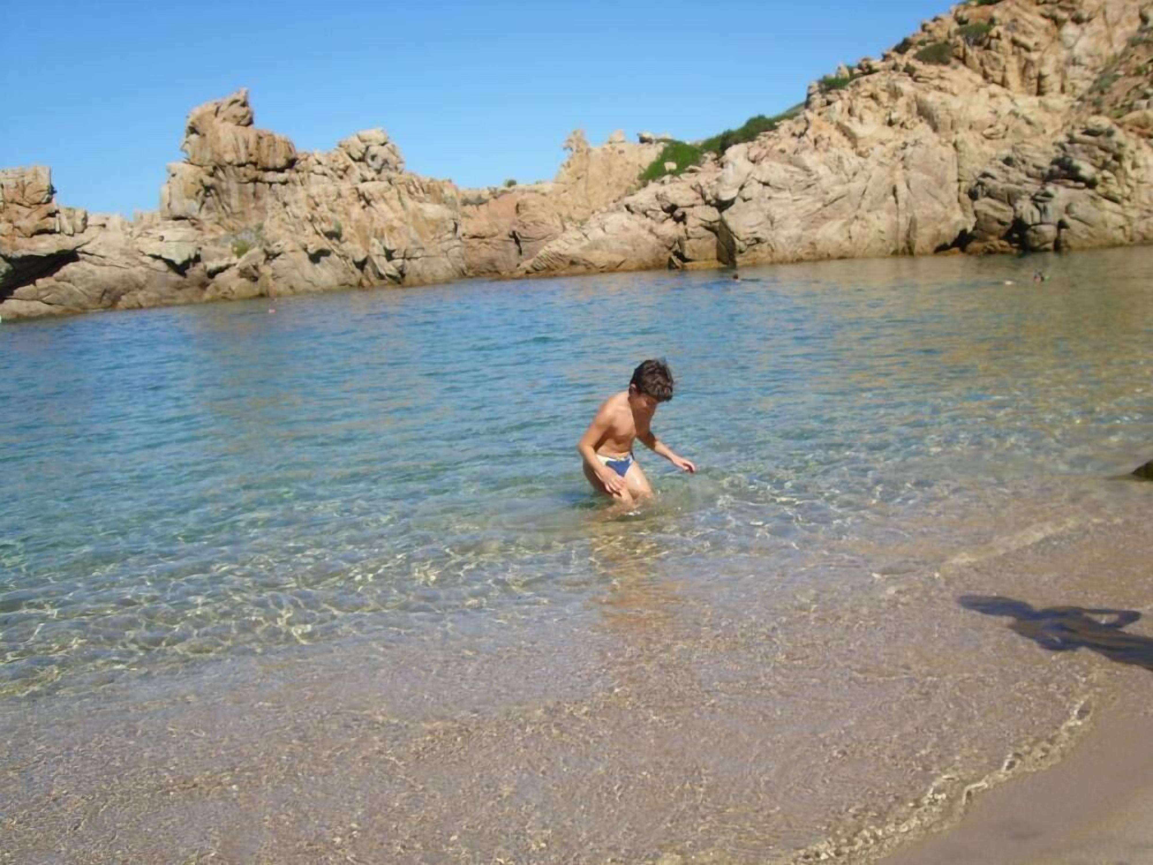 A child playing in shallow water near rocky cliffs.