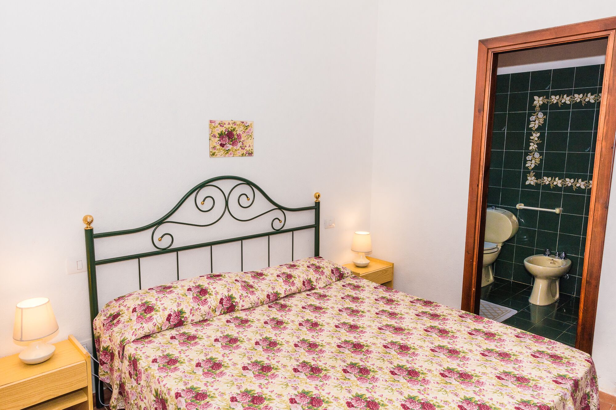 Un dormitorio con cama, mesita de noche, lámpara, espejo y puerta con un revestimiento de azulejos verdes.