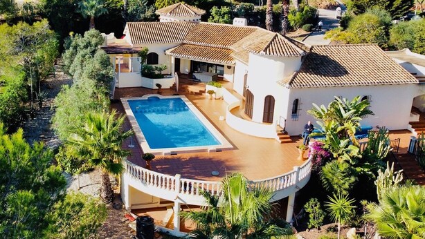 Une vaste villa dotée d’une piscine, entourée d’une végétation luxuriante et de palmiers.