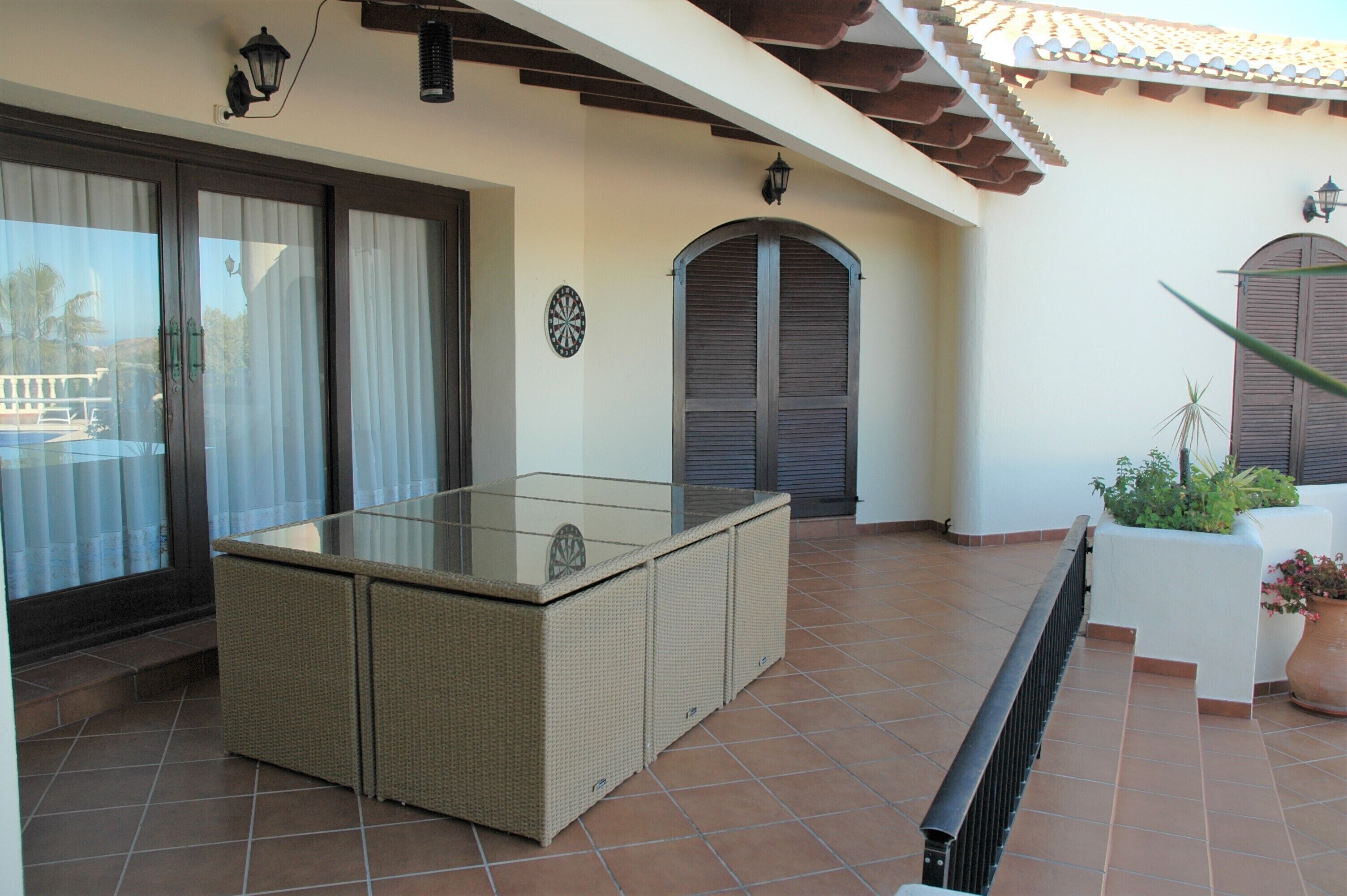 A patio area with a glass-top table, wicker furniture, and a potted plant.