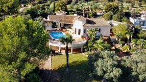 Une grande maison avec une piscine, entourée d’une végétation luxuriante et de palmiers.