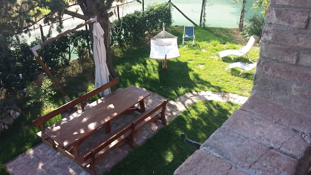 Un banco de madera y una mesa de picnic en un espacio al aire libre con césped, una cerca delimitando el área y una hamaca.