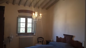 Un dormitorio con cama, radiador, ventana con cortinas, techo de madera y candelabro.
