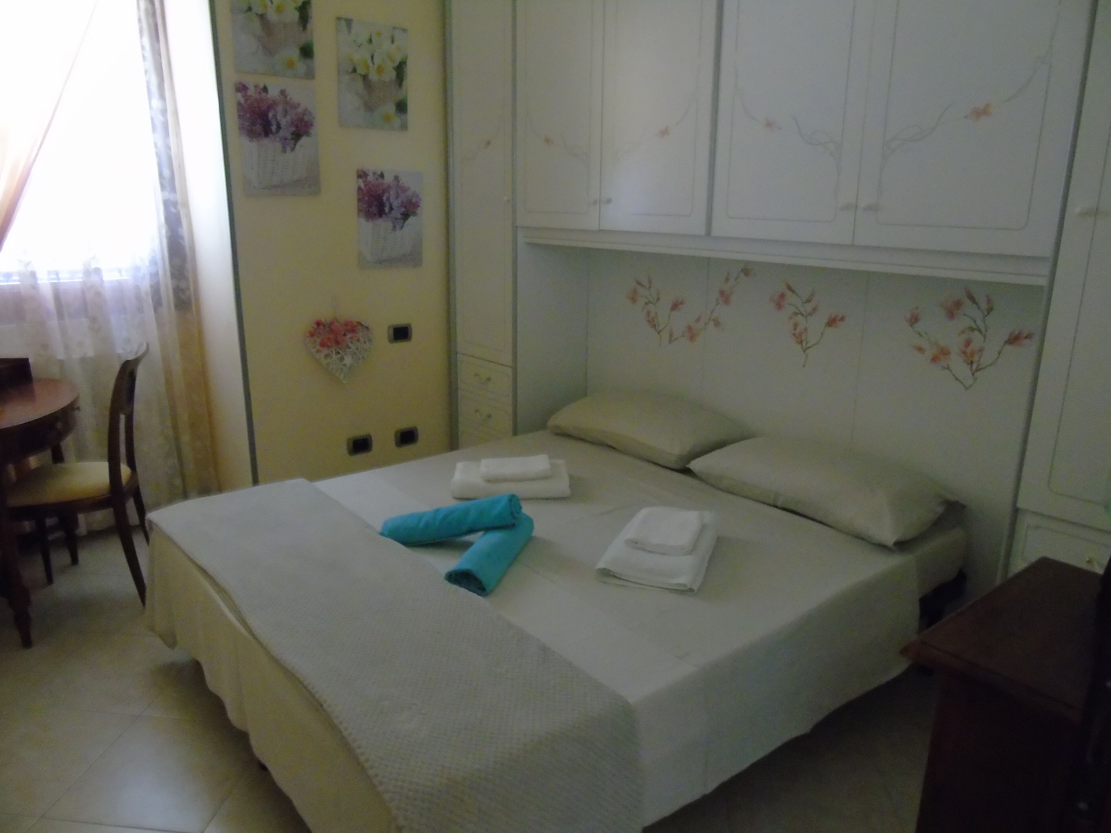 A neatly made bed with white linens and a blue towel, a small wooden table, and a chair.