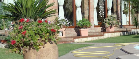 A large planter with various plants and flowers in front of a building with brick walls and large windows.
