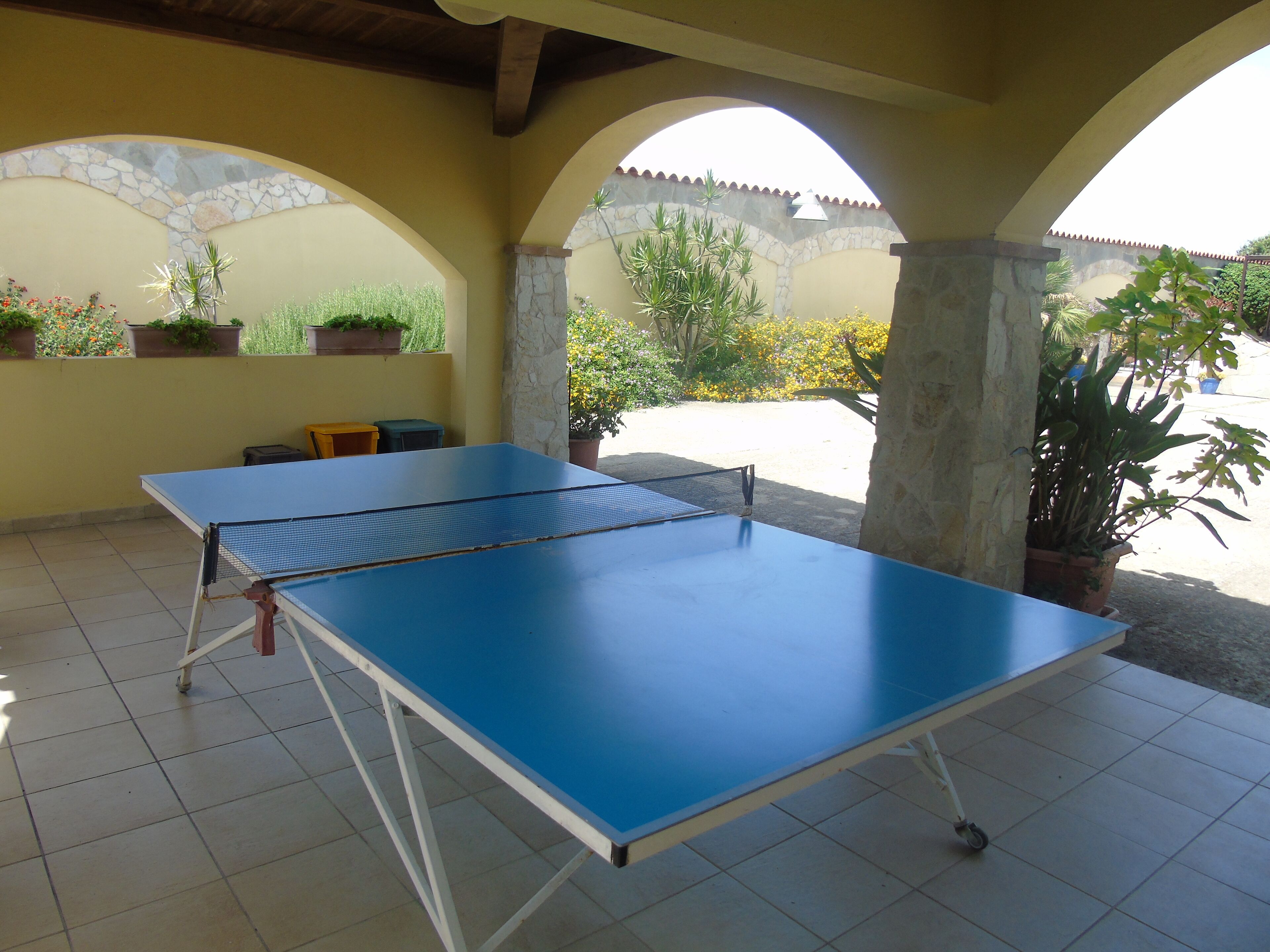 Une table de ping-pong installée dans un espace extérieur aménagé en patio, avec un sol carrelé et des piliers en pierre.