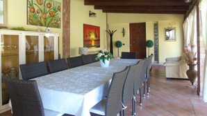 A dining area with a long table, wicker chairs, a cabinet with glass doors, and a painting of flowers on the wall. - Villa Graziosa (Quartu sant'Elena)