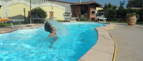 A swimming pool with a tiled edge, a lounge chair, and a patio area with a table and chairs.