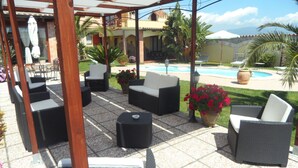 A covered patio area with outdoor furniture, a swimming pool, and a view of a building in the background. - Villa Graziosa (Quartu sant'Elena)