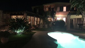 A nighttime view of a resort with a swimming pool, a covered patio, and a well-lit building. - Villa Graziosa (Quartu sant'Elena)
