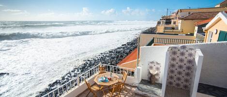 Een terras met uitzicht op zee, een tafel met stoelen en een betegelde muur.